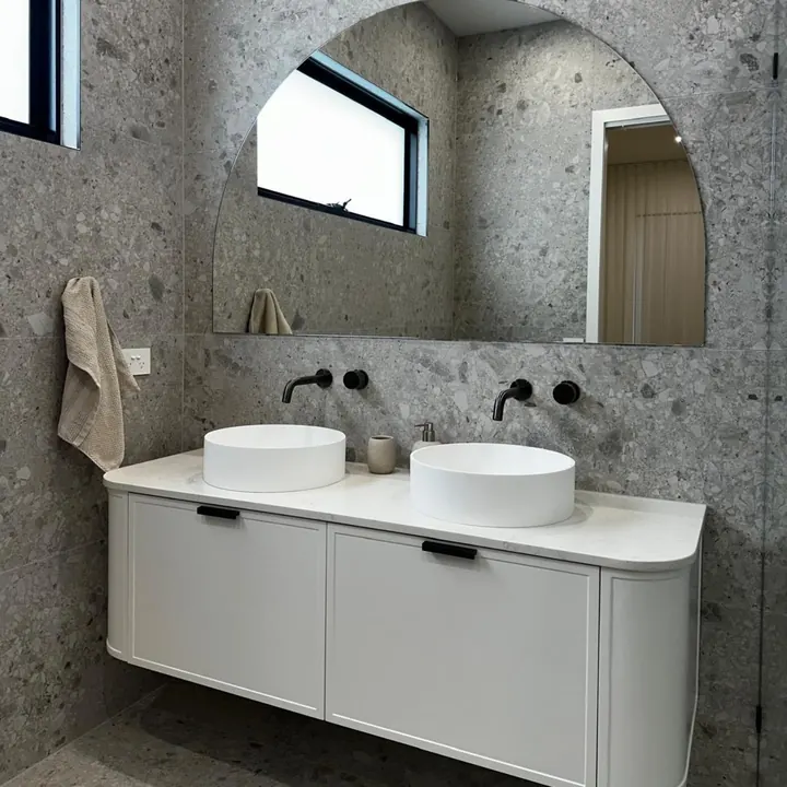 Curved white double vanity under an arched mirror
